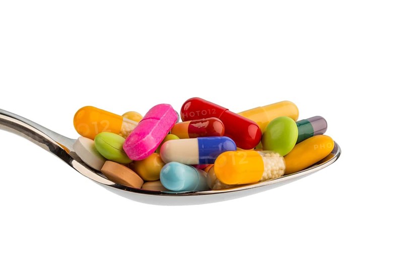 Lots of colorful tablets on a spoon. Symbolic photo for pill addiction and drug abuse
