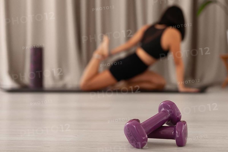 Close-up of purple dumbbells with a woman stretching in the blurred background