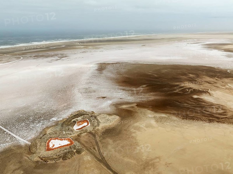 Saline ponds with ruddy algae growth and white salt deposits at the Atlantic Coast. Aerial view. Drone shot. Namib Desert, Skeleton Coast, Dorob National Park, Namibia