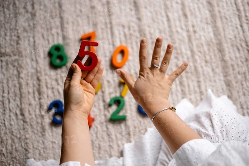 Hand showing number five with bright scattered numbers for learning