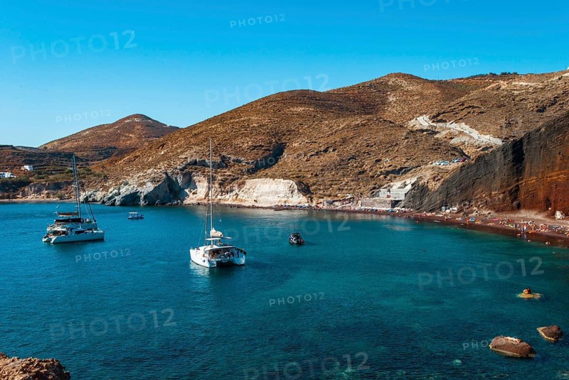 View of Kokkini Bay of Santorini's Red Beach, Tranquil coastal scene with boats on turquoise water near a rugged, mountainous shoreline under a clear blue sky, Santorini, Greece