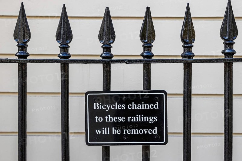 A black wrought iron railing bears a sign warning that bicycles chained to it will be removed