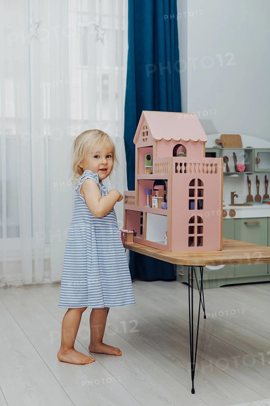 A young girl in a striped dress engages with a colorful dollhouse, smiling happily indoors