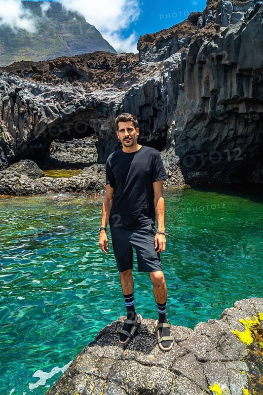 Man standing on volcanic rock by the emerald water of charco azul in el hierro, spain, enjoying a relaxing vacation surrounded by a unique natural landscape