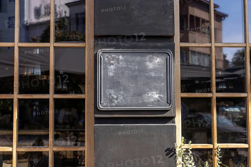A black blank chalkboard sign is displayed on the exterior wall of a restaurant, illuminated by the warm afternoon sunlight. Urban mockup for business, copy space, retro style window and wall