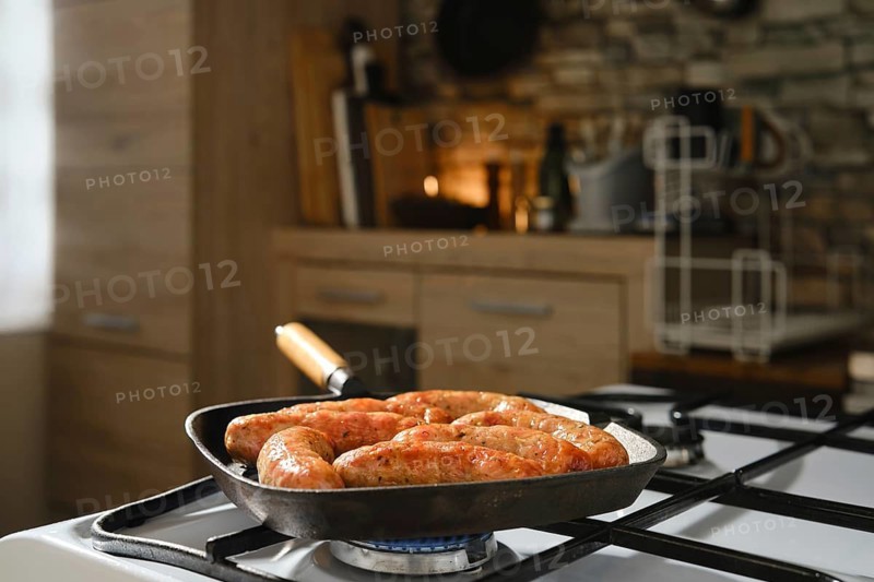 Homemade sausages in cast-iron skillet on gas stove. Grilling banger sausages in griddle pan at home