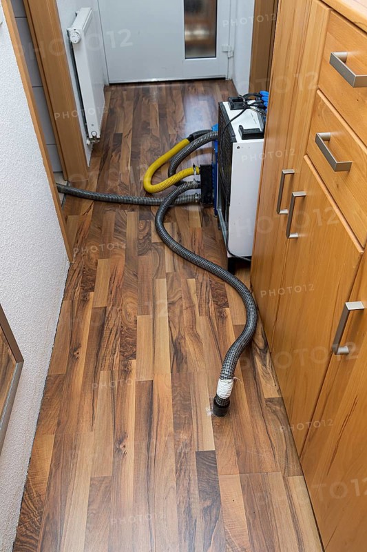 Professional water damage repair Drying equipment and hoses for underbody drying on wooden floor laminate