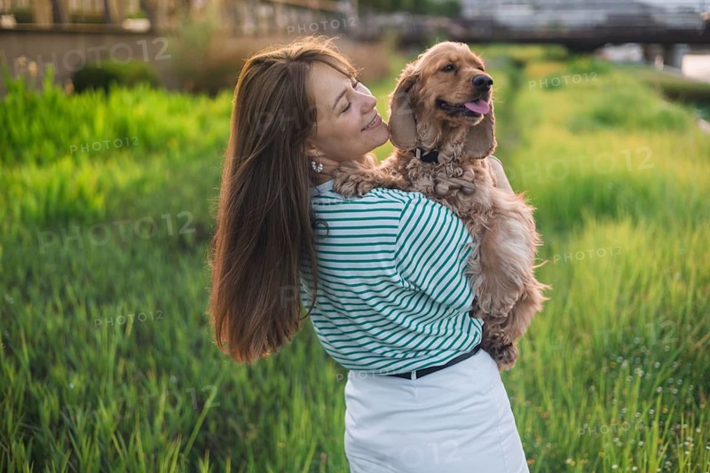 A woman holds her happy dog while standing in a field near mountains