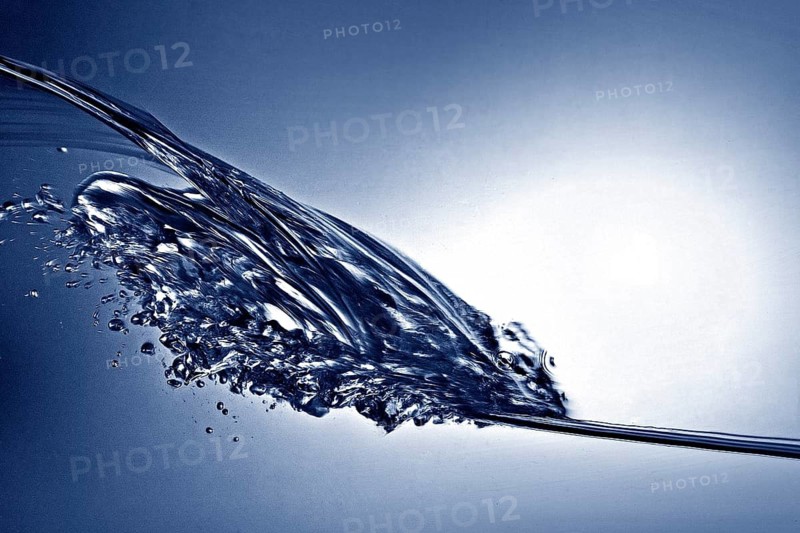 A small longitudinal wave frozen by short exposure in crystal-clear water in the photo studio in blue duplex toning