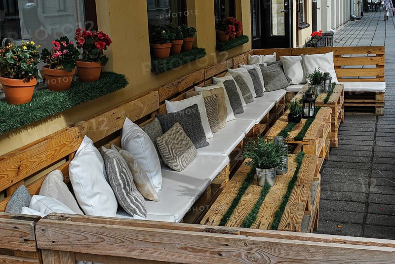 Summer Terrace Cafe with pillows and wooden pallets, outside restaurant terrace, Cozy outdoor seating area with wooden pallets, cushions, and plants lining a city sidewalk