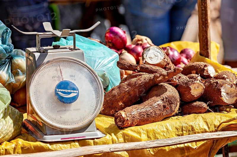 Market stand with cassava and onions on yellow cloth, next to a large scale, market scene in a small town in Caatinga in Bahia and Pernambuco in Brazil