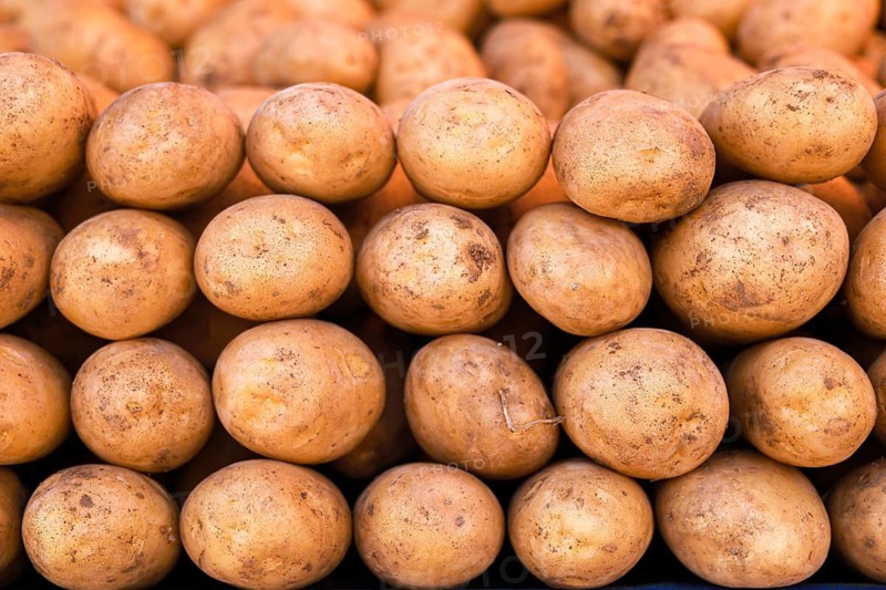 A neatly stacked pile of earthy brown potatoes