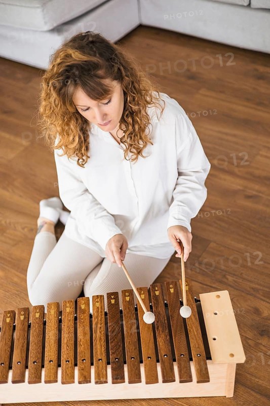 Woman playing a xylophone on a hardwood floor, focused and concentrated