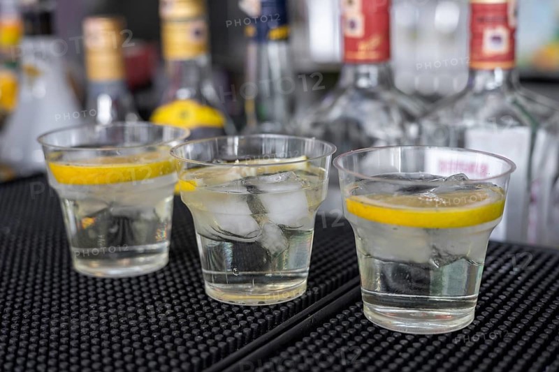Three glasses of chilled beverages sit on a bar counter, each garnished with a slice of lemon. The setting conveys a vibrant atmosphere typical of a hotel in Turkiye. cocktails in plastic glasses