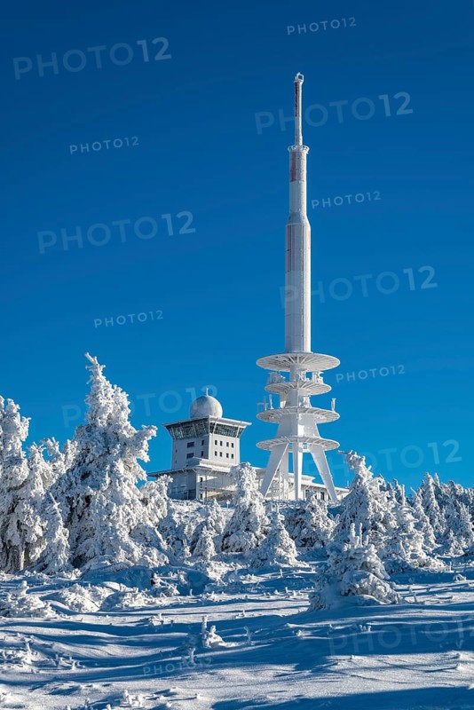 View over snow-covered spruce trees of the telecommunications tower and the radar station on the Brocken summit, on a sunny winter day under clear blue sky, Heinrich-Heine-Weg, Harz National Park, Saxony-Anhalt, Germany