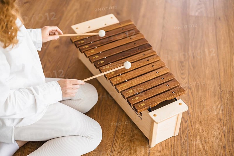 Woman playing marimba with focus, sitting on a wooden floor