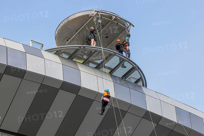 Three harnessed abseilers descend ropes from the circular viewing tower at Tottenham Hotspur Stadium, England, United Kingdom