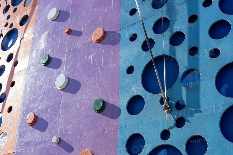 Tackling a colorful tall climbing wall tower. The setting offers a fun and engaging outdoor activity surrounded by vibrant architecture. Activities and sport training for children