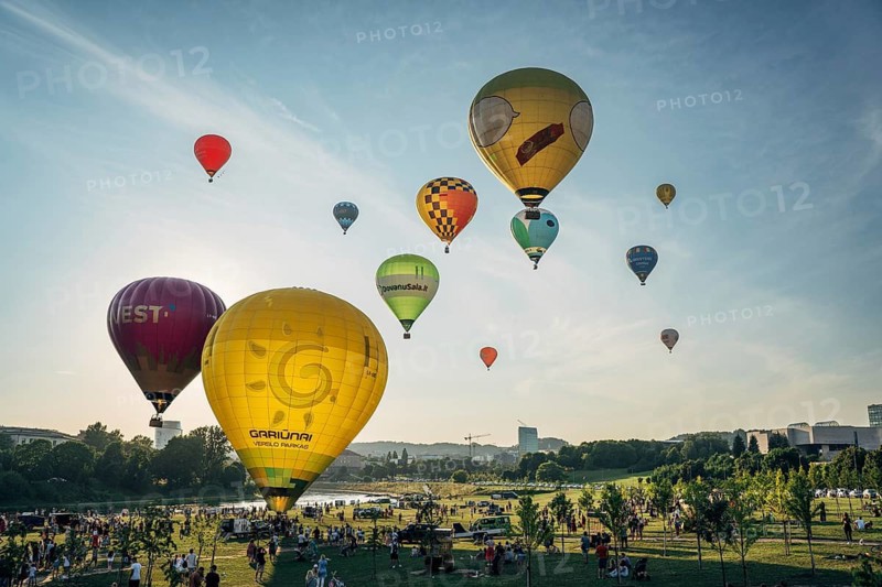 Vilnius, Lithuania, 08 05 2022: Hot air balloons in Vilnius. Multi-colored hot air balloons on the ground before takeoff. Lots of balloons in the field, Hot air balloons soaring over a green park with spectators watching at sunset, creating a vibrant scene, Vilnius, Lithuania