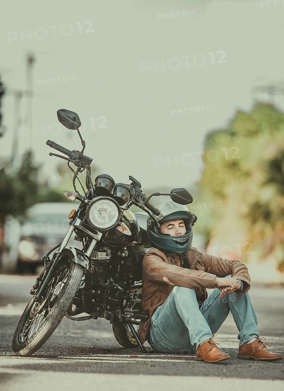 Male motorcyclist in jacket sitting leaning to his motorcycle on the road