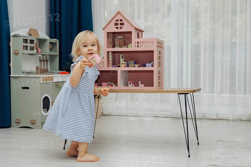 Child girl in blue dress arranges wooden furniture in a doll house. Concept of education during the game