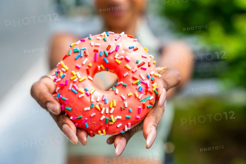 Hands presenting a delicious vibrant doughnut topped with bright pink icing and colorful sprinkles, symbolizing sharing, joy, and the indulgence of a sugary treat for celebration