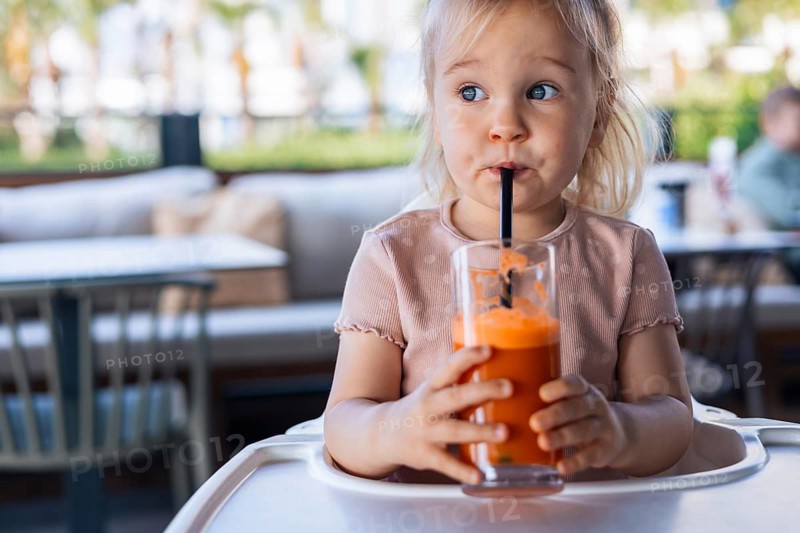 Girl toddler drinking fresh orange carrot juice in outdoor cafe