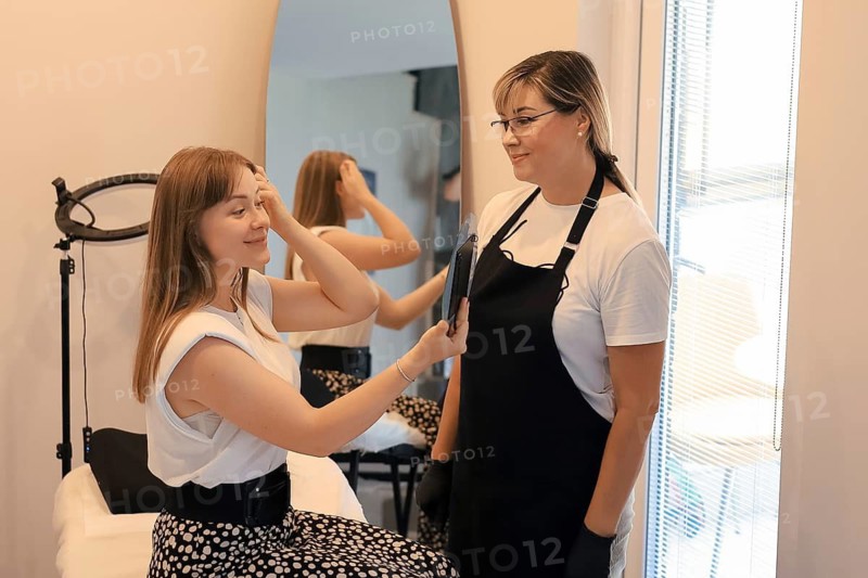 A woman views her reflection with a hand mirror while the stylist watches