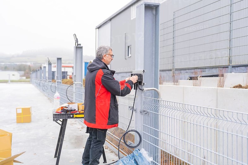 A worker in jacket and red works an outdoor railing with a drill, parking garage construction, Calw, Germany