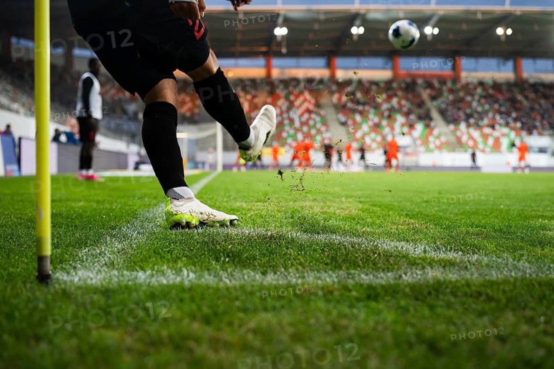 Close-up of soccer player kicking a football on a professional grass field, capturing dynamic sports action with stadium and spectators blurred in background in Lubin, Poland