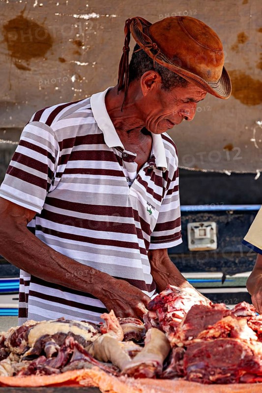 Man in traditional clothing cuts up concentrated meat on a slaughter table, market scene in a small town in the Caatinga of Bahia and Pernambuco in Brazil