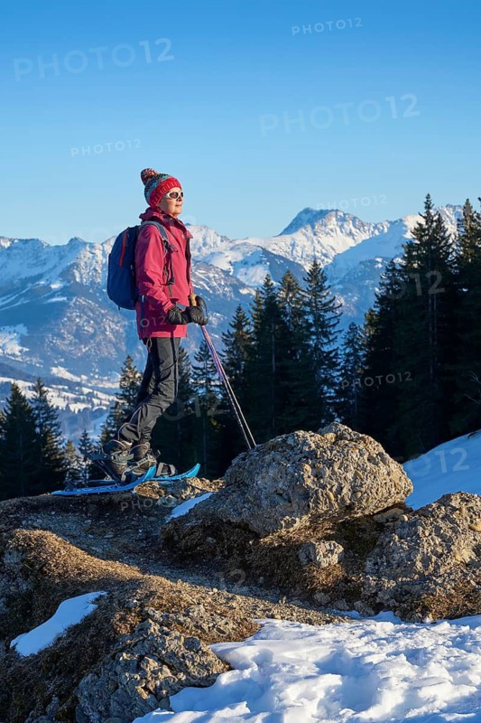 Nice and active senior woman snowshoeing in in the snow covered Allgaue alps above the valley of river Iller, Immenstadt, Bavaria, Germany