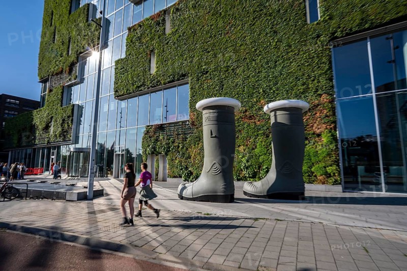 Work of art The Boots of the Hunter, sculpture of 2 large rubber boots that glow in the evening, by Venlo artist Pii Dänen, in front of the green north façade of Stadskontoor Venlo, building of the city administration, from 2016, approx. 2200 square meters of the façade are green, various types of plants hang in plant modules in front of the actual façade, a combined climate concept, a circulatory system, with a greenhouse on the upper floors, thermal energy from The underground parking garage, a so-called solar chimney, cools the building air in summer and heated in winter, rainwater is used to irrigate the green building façade, the entire project was built according to the cradle-to-cradle concept, Venlo, Limburg, the Netherlands