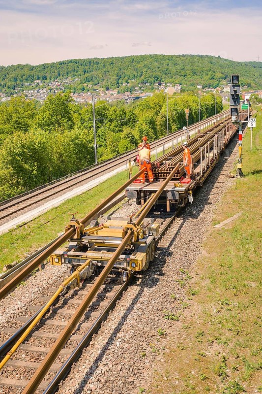 Workers wearing orange clothing working on tracks in a tree-lined hillscape, Leonhard Weiss construction site to renovate the train station and build the overhead line, Waldshut, Germany