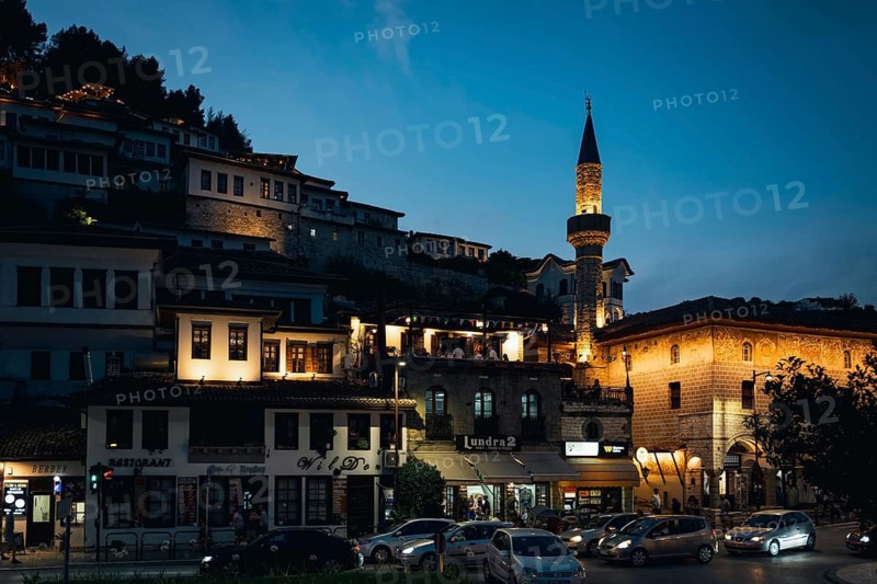 BERAT, ALBANIA - JULY 2, 2026: Illuminated streets and traditional Ottoman buildings at night with a glowing Kindom mosque minaret under a deep blue sky