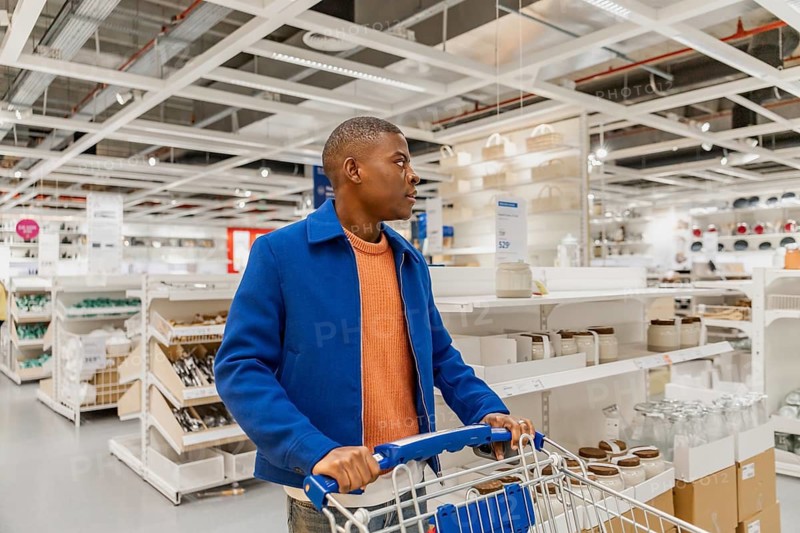 A person is shopping in a home goods store. They are looking around while pushing an empty cart. The store has many shelves and products on display