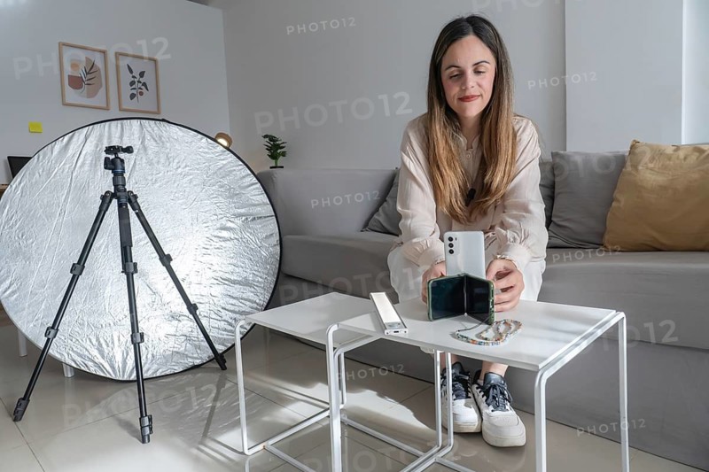 Close up of woman placing smartphone into a small phone stand on coffee table, beaded phone strap and LED light panel visible beside her