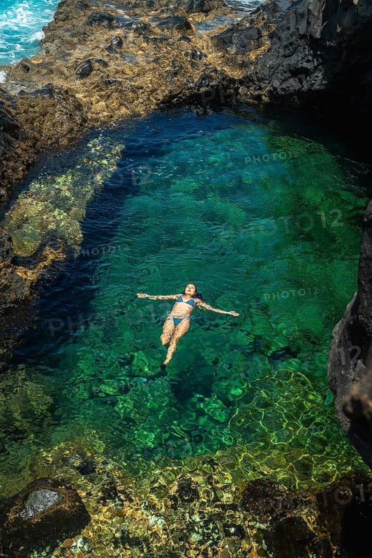 Woman in a blue bikini enjoying vacation, floating effortlessly on her back in a volcanic natural pool with clear turquoise water surrounded by dark rocks on el hierro island