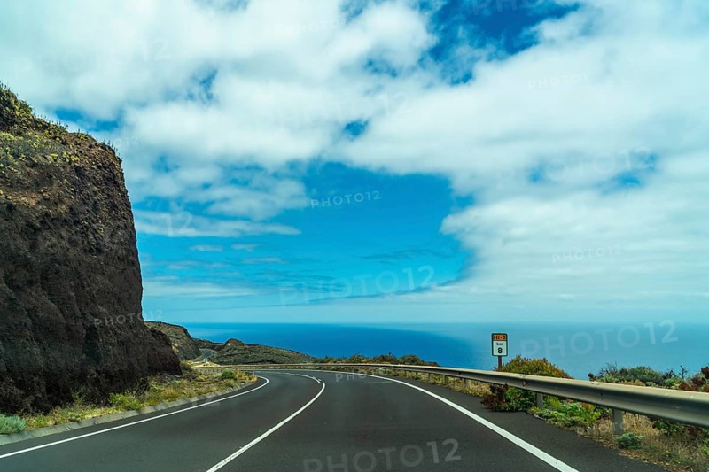 Scenic highway following the rugged coastline of el hierro in the canary islands, offering expansive views of the blue atlantic ocean under a bright sky with white clouds