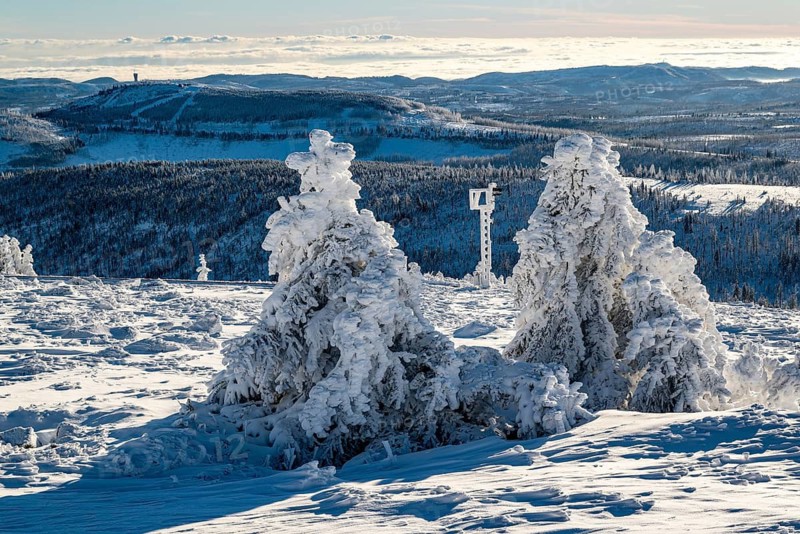 Panoramic view of the railway line and bizarrely shaped spruce trees covered by snow and ice on the summit of Mount Brocken over the winter landscape of the Harz with mountains and forests, on a sunny winter day under clear blue skies, Harz National Park, Saxony-Anhalt, Germany