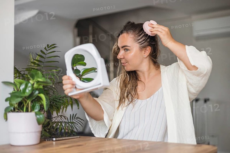 Woman, aking sculp head massage and applying hair product while looking in a mirror in a modern indoor setting