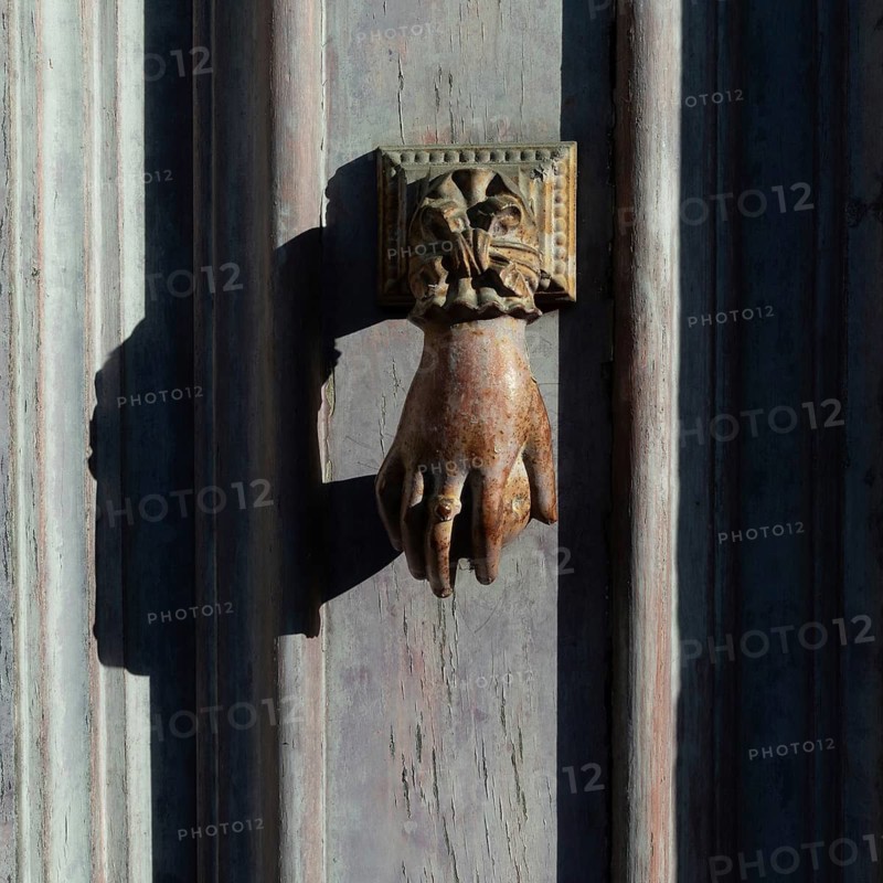 Antique hand door knocker on weathered wooden door