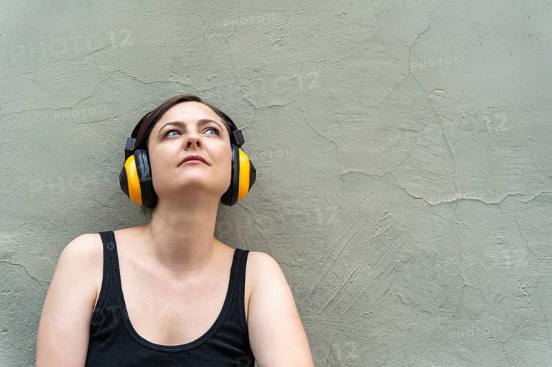 Blonde woman 40s in yellow headphones lost in music, close-up urban portrait, A woman with headphones leans against a concrete wall, looking upwards in a relaxed state