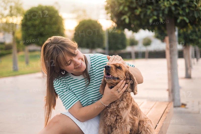 A woman affectionately petting her dog on a bench in a warmly lit park