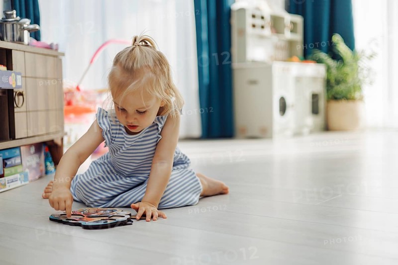 Child girl toddler enjoys a colorful puzzle on the floor while surrounded by soft light and greenery