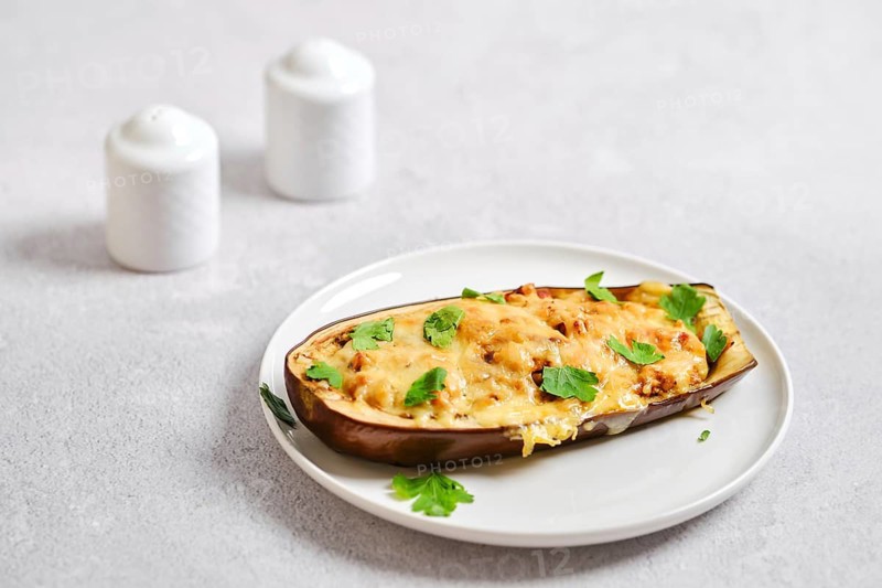 Cheesy baked eggplant with mincemeat sits on white plate. Herbs are sprinkled on top. Salt and pepper shakers are on simple kitchen countertop