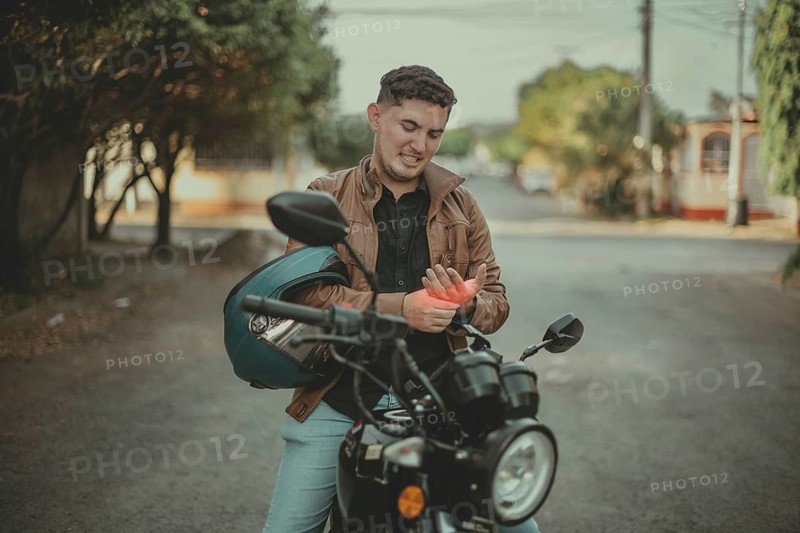 Young motorcyclist suffering from arthritis pain on the road. Motorcyclist with hand pain on the street