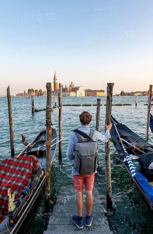 Young man at a boat dock for Venetian gondolas in St. Mark's Square, tourist enjoying the evening, back church of San Giorgio Maggiore in the evening light, Venice, Veneto, Italy