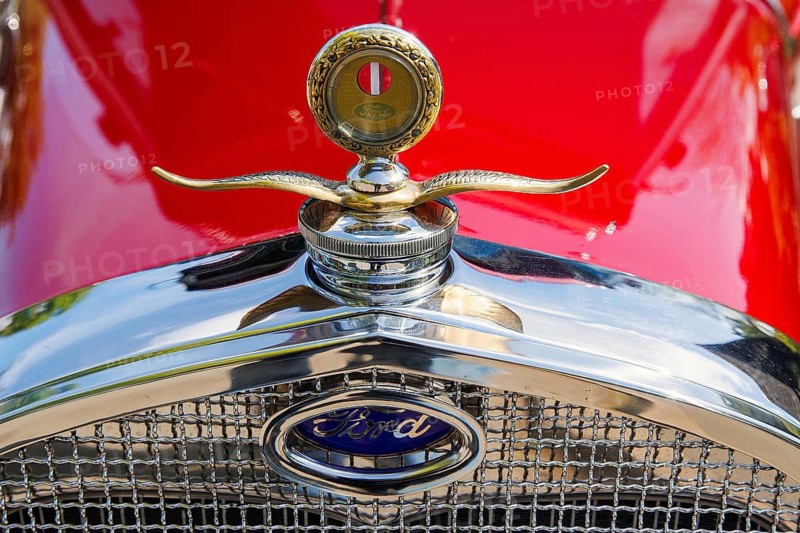 Winged radiator mascot and Ford badge on a red vintage car at a classic car meet