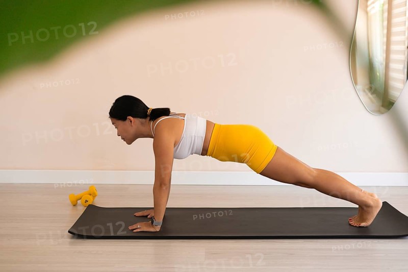 Woman in a plank position on a mat, decorated with greenery